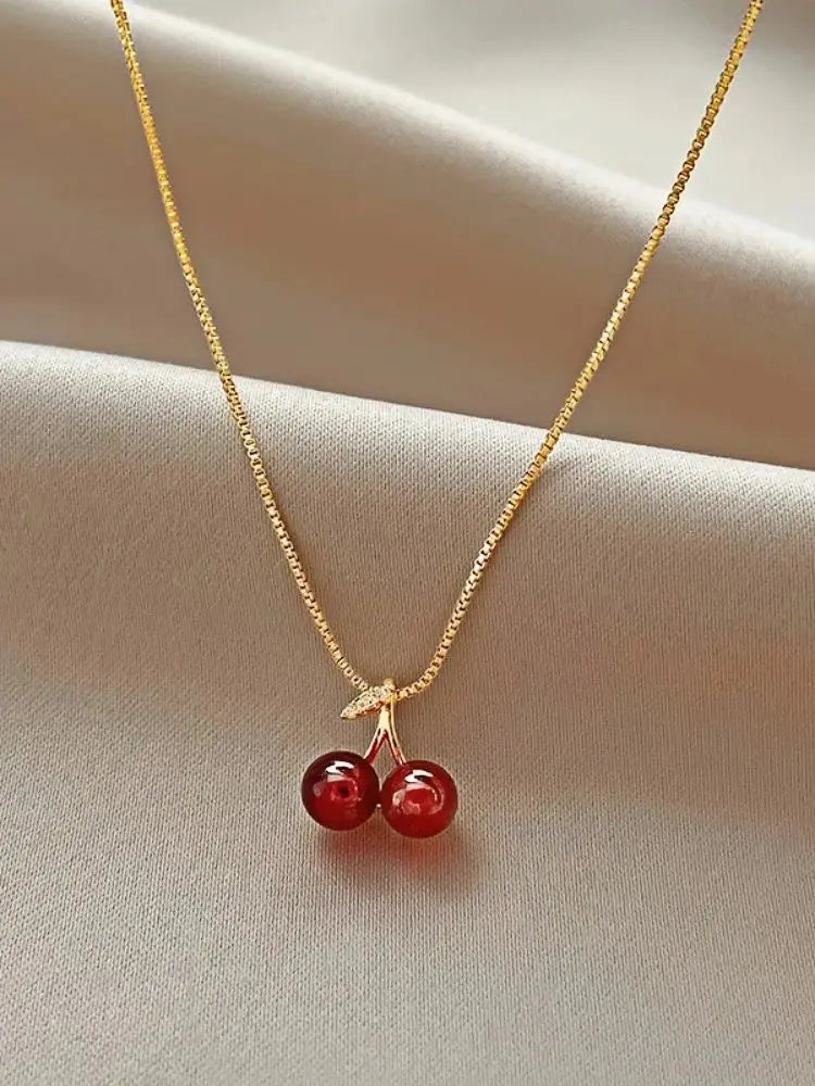 Collana dorata con ciondolo a ciliegia rosso vino, femminile e vivace, perfetta per feste e come regalo.