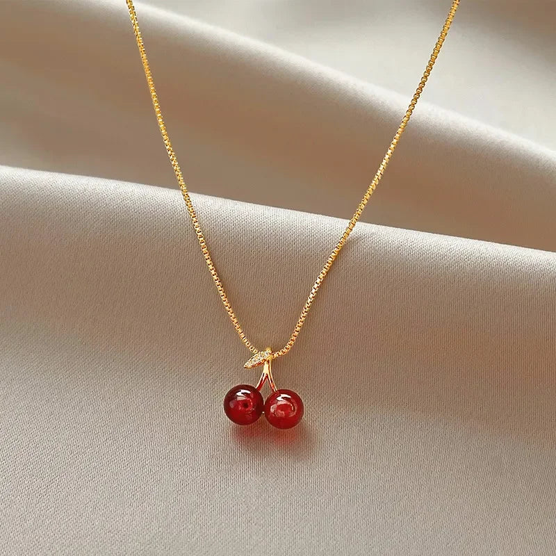 Collana dorata con ciondolo a ciliegia rosso vino, femminile e vivace, perfetta per feste e come regalo.