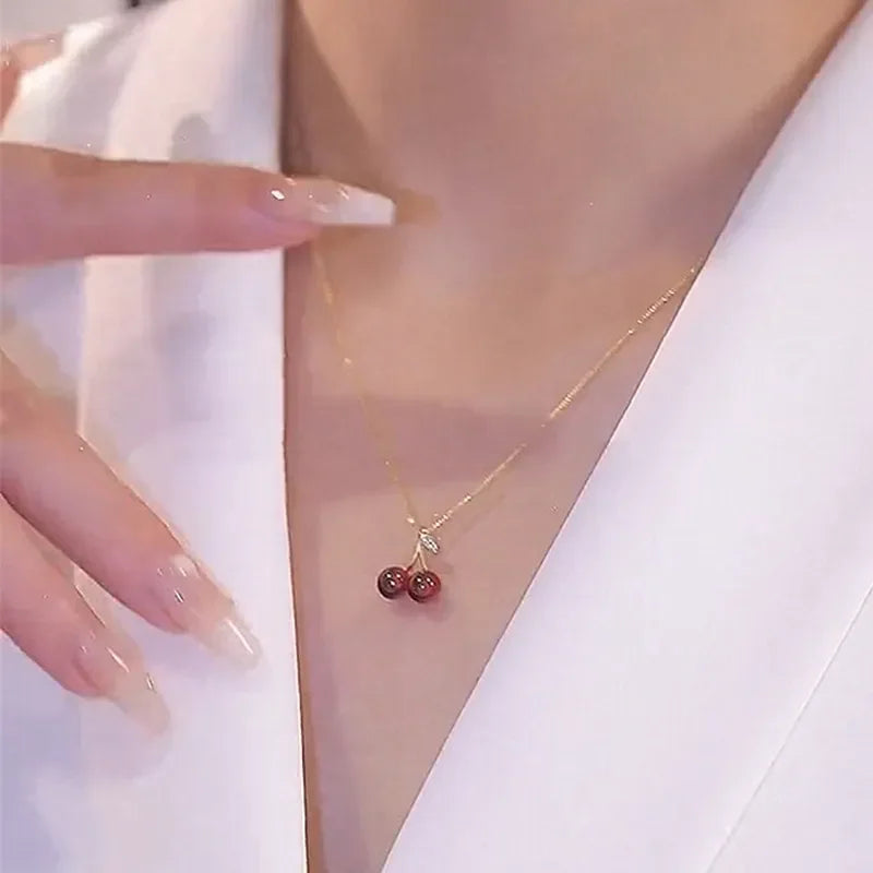 Collana dorata con ciondolo a ciliegia rosso vino, femminile e vivace, perfetta per feste e come regalo.