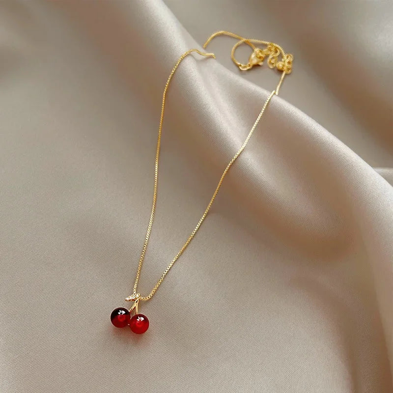 Collana dorata con ciondolo a ciliegia rosso vino, femminile e vivace, perfetta per feste e come regalo.